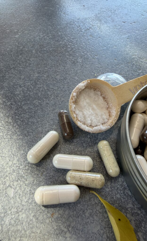 Verschiedene Magnesium-Präparate: Kapseln in unterschiedlichen Farbtönen sowie ein Messlöffel mit Magnesiumpulver auf einer Steinoberfläche