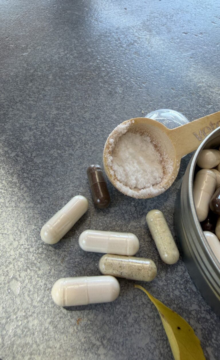 Verschiedene Magnesium-Präparate: Kapseln in unterschiedlichen Farbtönen sowie ein Messlöffel mit Magnesiumpulver auf einer Steinoberfläche